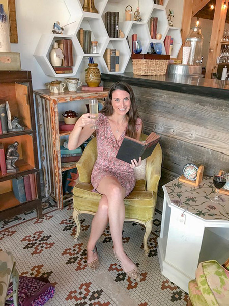 Christine, a brunette white female in a pink dress sitting with wine and book