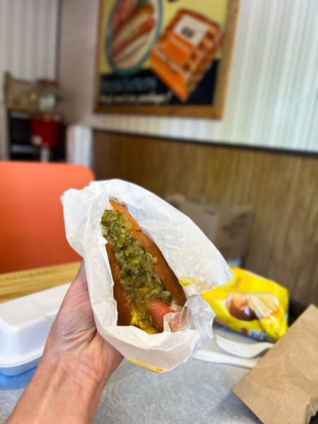 Hot Dog World Hendersonville Restaurant NC with white hand holding a hot dog with relish and onions in booth with orange seats