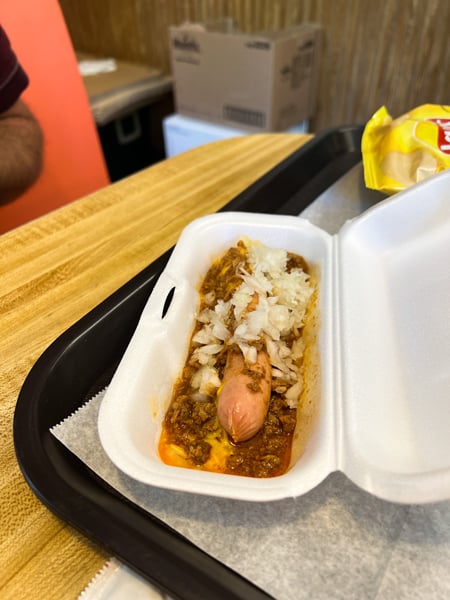 Hot Dog World Restaurant Hendersonville NC with bun-less hot dog with chili and onions in a styrofoam container on table with orange booth chairs