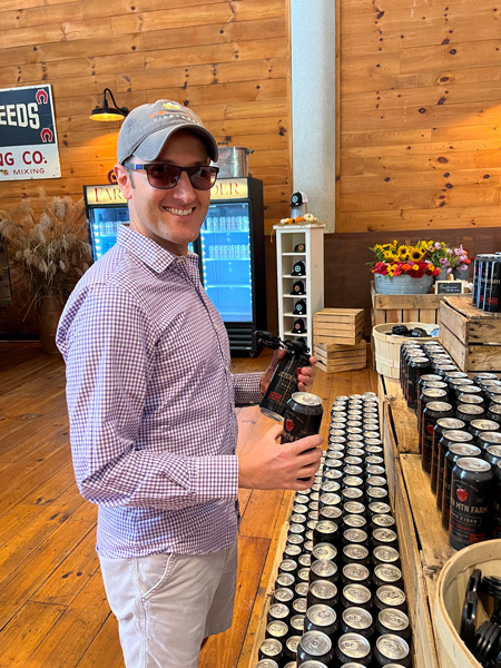 Jeter Mountain Farm Cider Hendersonville NC with white male in gray hat with purple shirt making a 4 pack of cider in country store