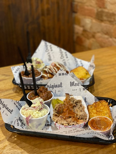 Moe's Original BBQ Hendersonville NC with two plates of BBQ in black baskets with paper filled with smoke chicken, pulled pork, potato salad, and baked beans
