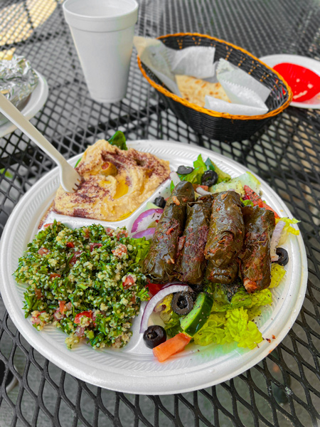 Pita Express Restaurant Hendersonville NC with styrofoam plate with grape leaves, salad with tomato and olives, and hummus with pita