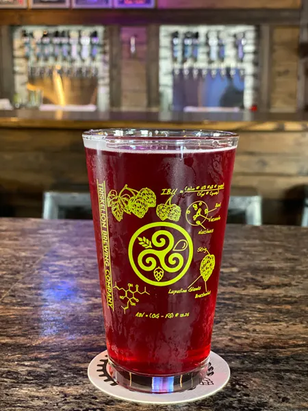 Triskelion Brewing Hendersonville Brewery red cider in beer glass with bar blurred in background