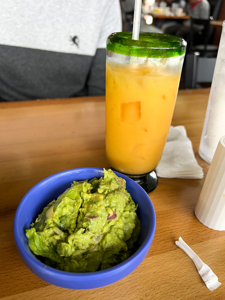 Ay Caramba in Asheville NC Guacamole in blue bowl next to orange cocktail on brown table