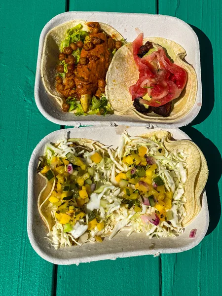 Best tacos Asheville white duck taco shop with two plates of two tacos each with colorful toppings on top of a green picnic table