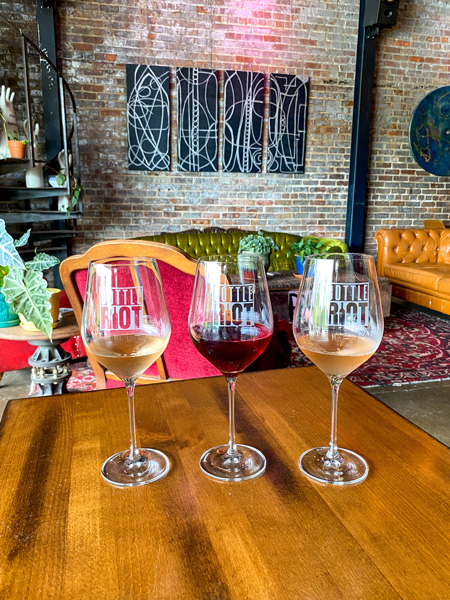 Bottle Riot Wines Asheville with three glasses of half-pour red and white wines on table