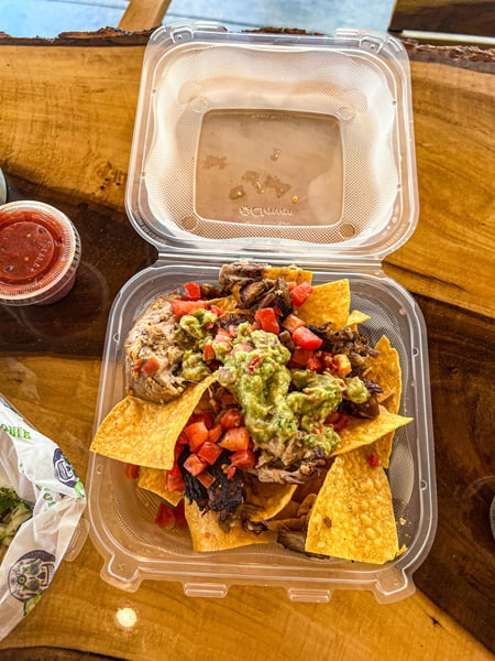 Cantina Louie Asheville NC Nachos with corn chips, black beans, tomatoes, onion, and carnitas in takeaway container on wood table