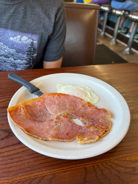 Five Points Restaurant Asheville NC Breakfast with large white plate on brown table with large slice of thin ham steak and one over easy egg