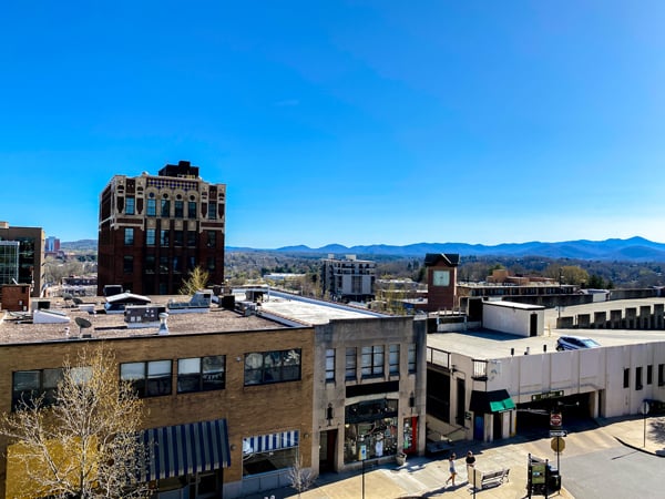 Hemingways Cuba Rooftop Bar Asheville with views of Downtown Asheville buildings, bright blue sky, and the Blue Ridge Mountains