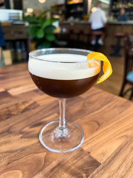 La Bodega Curate Asheville Cocktail with brown liquid and orange or lemon zest garnish on brown table