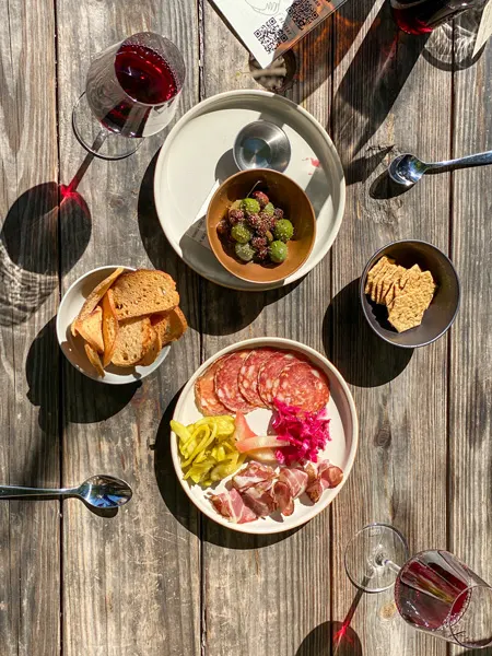 Leos House Of Thirst Sunday Brunch West Asheville with plates on picnic table including olives, crackers, and charcuterie with two glasses of red wine