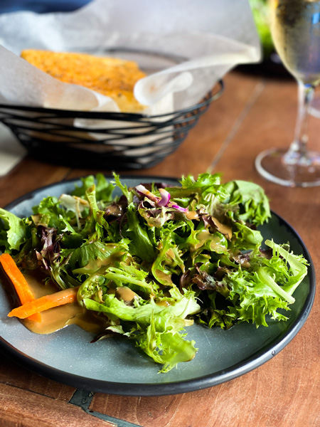 Nine Mile Restaurant Asheville NC with plate of salad with carrots, bread basket, and glass of white wine