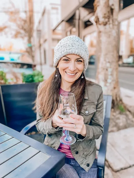 Outdoor patio Walls Wine Bar Asheville NC with white brunette female drinking wine with white white, purple shirt, and green jacket on at table