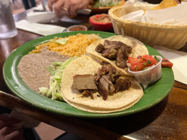 Papas and Beer Mexican Restaurant Asheville NC with green plate filled with rice, brown beans, and two soft corn tacos with carnitas and pico de gallo on the side