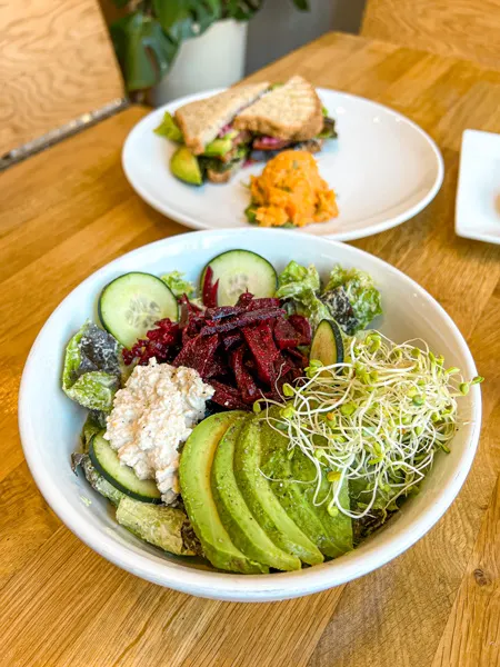 Pulp and Sprout Asheville Breakfast Bowl with avocado, sprouts, beets, and cucumber and sandwich on plate behind it