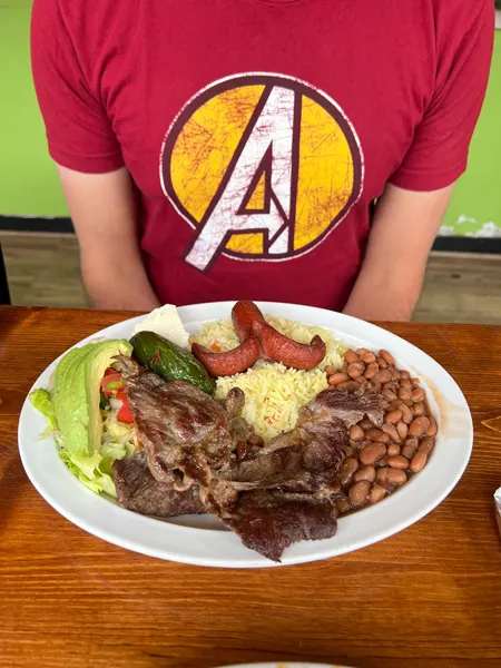 Pupuseria Patty Restaurant Asheville NC with white male sitting in front of white plate of food with beans, sausage, meats, and lettuce
