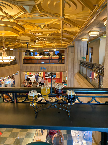 S&W Market Asheville Food Hall with flight of Highland Brewing beer from second level overlooking food stalls and people