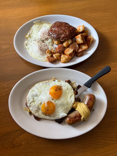 Sawhorse Restaurant Asheville Breakfast with two white plates filled with sausage, eggs, potatoes, and Brussels sprouts