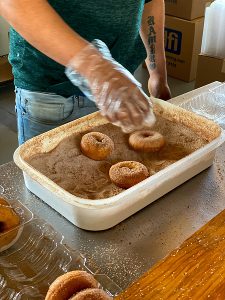 Sky Top Orchard Apple Cider Donuts being coated in cinnamon and sugar