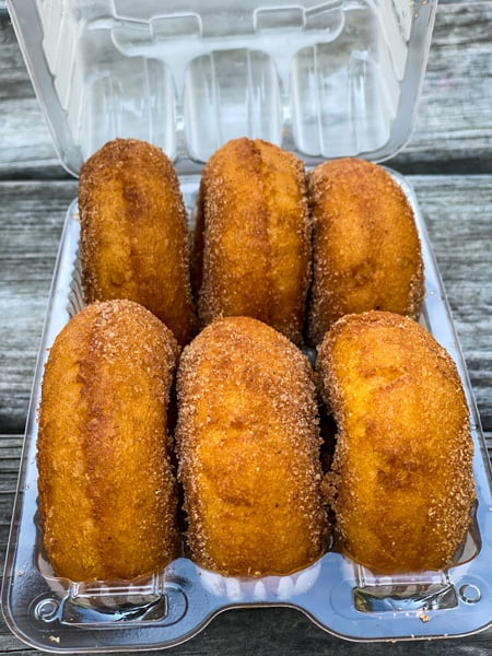 Sky Top Orchard Donuts with 6 brown donuts in a plastic container on a picnic table