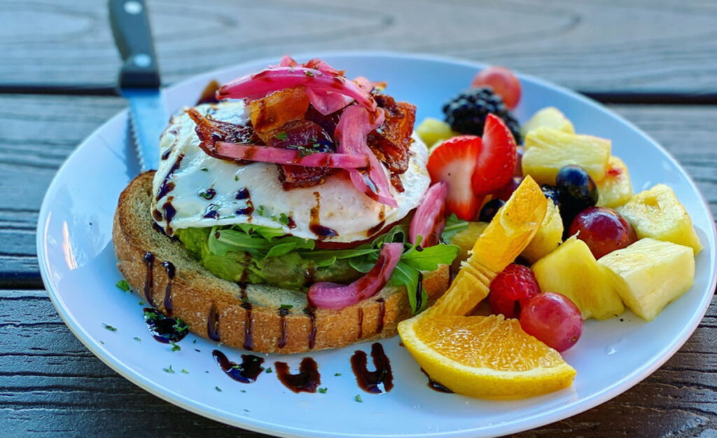 Plate filled with open-faced egg and avocado sandwich with pickled onions and side of fruit for breakfast in Asheville, NC at local Sunny Point Cafe