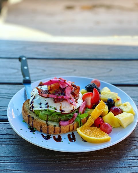 White plate filled with avocado toast, egg, bacon, and fresh fruit like orange slice, blueberries, and strawberries at Sunny Point Cafe in West Asheville