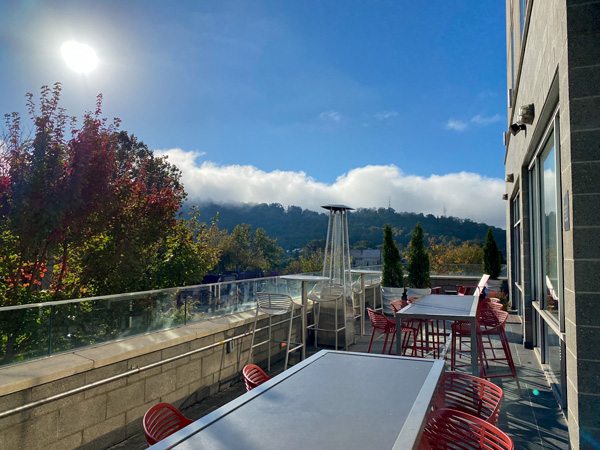 The Ledge Aloft Rooftop Bar Asheville with silver tables and red orange chairs with fall foliage, blue sky, and sun