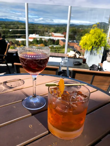 The Montford Rooftop Bar Asheville with two cocktails overlooking Asheville sky line and Blue Ridge Mountains