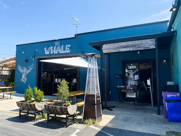 The Whale West Asheville North Carolina with blue building with patio, umbrella, and chairs with whale tail mural on wall