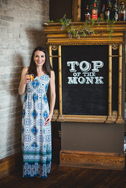 Top Of The Monk Rooftop Bar downtown Asheville NC with sign and white brunette woman in blue and white dress holding a cocktail