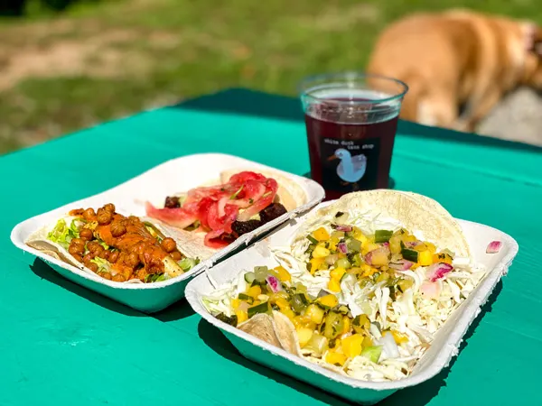 White Duck Taco Shop Asheville Tacos with Ginger Revenge ginger beer and four soft shell tacos on green picnic table outside
