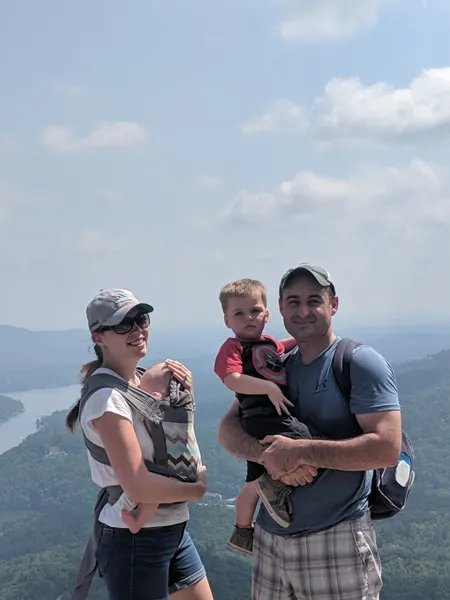 Chimney Rock Hiking With Kids with white male and female holding two young children overlooking mountains