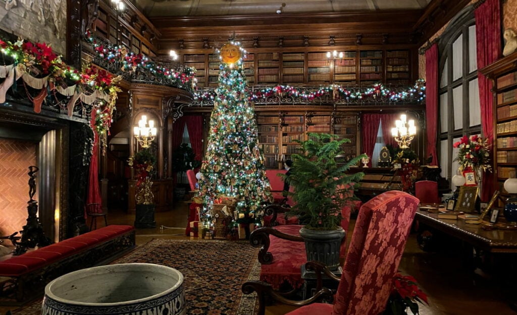 Biltmore Estate's library with bookshelves and fireplace lit and decorated with wreaths, garland, and holiday trees for Christmas in Asheville, NC