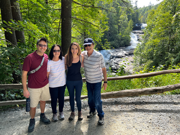 DuPont State Forest Triple Falls Waterfalls with group of four white brunette family members posing in front of the three-tiered waterfall