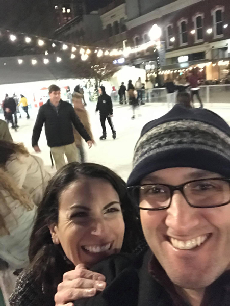 White brunette female and male in winter coats taking a blurry selfie on the ice skating rink in Knoxville, TN with people also skating behind them