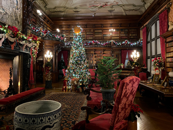 Biltmore Estate Christmas Decor Library with Christmas tree, garland hanging from library bookshelves, and glowing fireplace