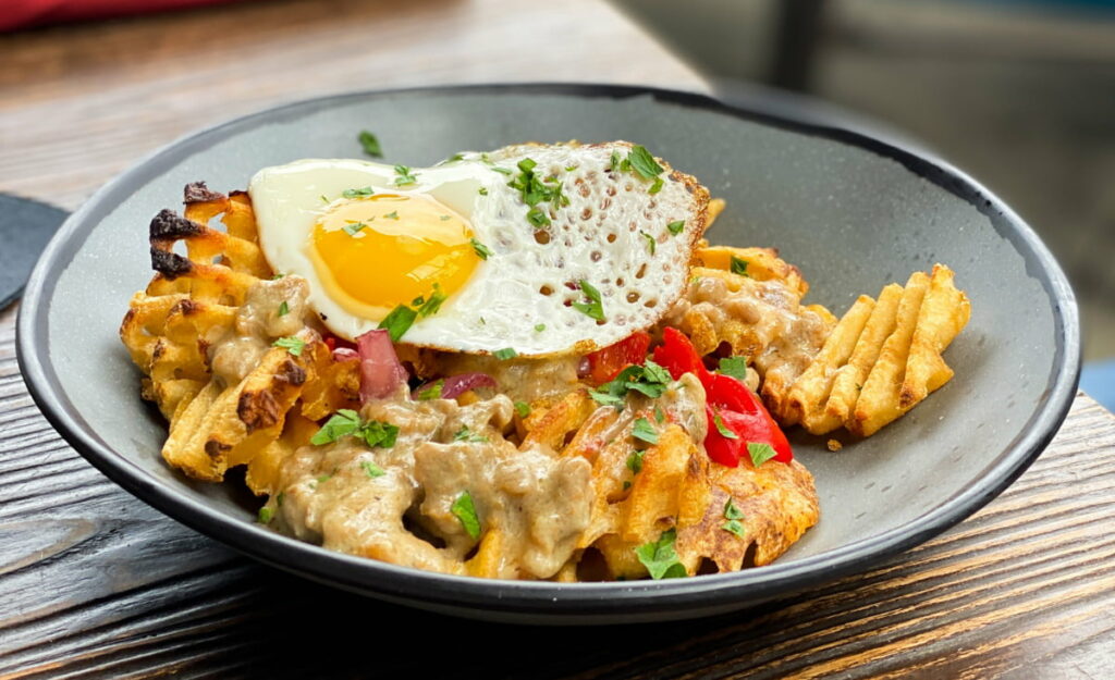 Bowl filled with a sunny side up egg, waffle fries, and pickled on for brunch In Asheville NC at Social Lounge, a rooftop restaurant downtown