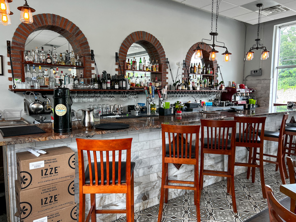 Cecilia's Kitchen in Asheville NC Bar with four brown chairs, three arched mirrors, and wall of glassware and liquors