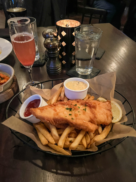 Cedric's Tavern at Biltmore Estate in Asheville with fried cod fish and chips in basket on table with cocktail and candle in the background