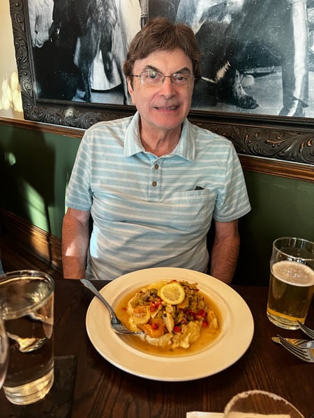 Older white male with brown hair in blue striped shirt with plate of food at Cedric's Tavern