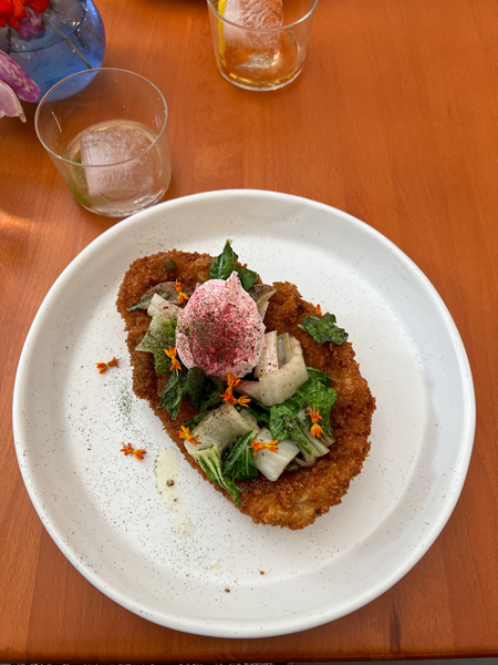 ELDR Restaurant Asheville NC Schnitzel with egg, beet shavings, and bok choy on white plate next to cocktail glasses on brown table