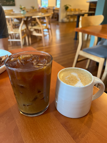 ELDR Restaurant Coffee Asheville NC with iced coffee and latte in white cup on brown table and restaurant table and chairs in the background