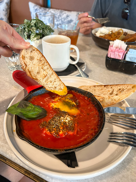 Gemelli Restaurant in Asheville breakfast dish with white hand dipping bread into red sauce with poached egg on top