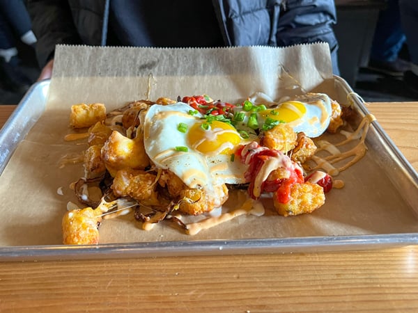 Brunch platter with two sunny side up eggs, tater tots with ketchup, and green herbs at Haywood Common in Asheville NC