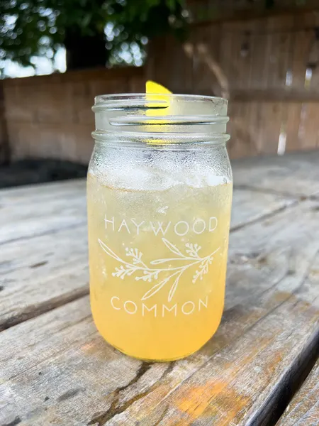 Haywood Common Asheville North Carolina yellow cocktail with ice in mason jar garnished with lemon on outdoor picnic table