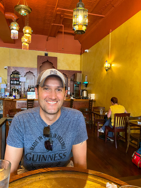 Jerusalem Garden Cafe Downtown Asheville NC brunch with white male in blue shirt with hat and colorful lamps hanging from ceiling