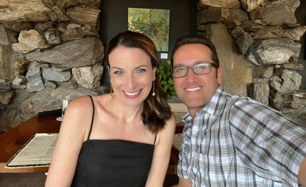 Featured "Most Romantic Restaurants In Asheville For Date Night" article image with Christine and Tom, a white brunette male and female taking a selfie at their table at The Omni Grove Park Inn's Restaurant, Edison