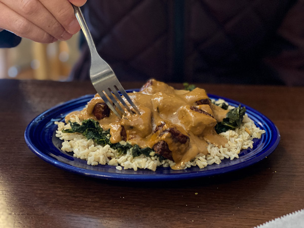 Rosettas Kitchen Vegan Food Asheville NC with blue plate filled with kale, rice, and peanut butter tofu with sauce and fork about to it