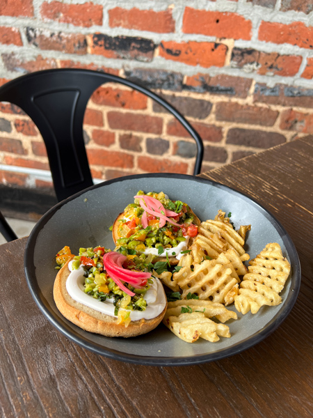 Social Lounge Sunday Brunch Downtown Asheville NC with vegan English muffins, waffle fries, vegan sour cream, and pickled veggies on blue-gray plate on brown table on rooftop with brick wall in background