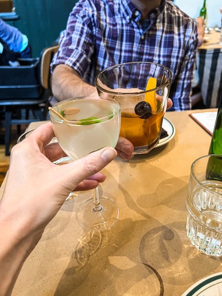 White male and female hands doing a cheers with craft cocktails (a martini and old fashioned) at Tall John's restaurant in Asheville, NC